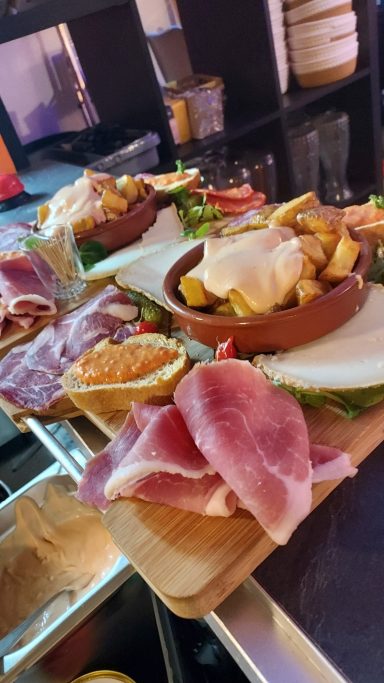 Plateau de charcuterie avec jambon, salades, fruits et sauces en accompagnement.